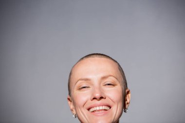 Gri arka plan duvarında kendine güvenen güzel, mutlu, kel bir kadın.