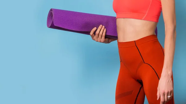 Sporty yoga girl with yoga mat wearing sportswear isolated over blue background, copy space