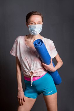 Ukrayna, Kyiv- 01 Nisan 2020: koruyucu maske takan ve yoga minderi tutan beyaz kadın. Zevk konseptiyle karantina zamanı. Koronavirüs yüzünden karantina altında.