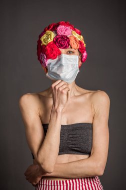 Tıbbi maskeli yapay çiçek şapkası takan kadın gri arka planda izole edilmiş. Boşluğu kopyala