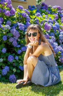 Yeşil parkta, yaz elbisesinde oturan güzel bir kadın. Çiçekli hidragea çalılarının üzerinde. 