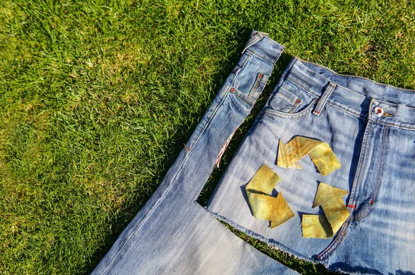 緑の草の上にデニム生地のリサイクルシンボル 古いですボーイフレンドジーンズから新しいスカート — ストック写真
