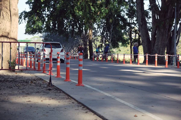 Traffic regulation pole and rumble strip on asphalt road in public park with people exercise background in the evening of sunny day. The symbol of safety first.