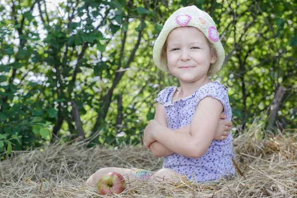Kleines Bauernmädchen sitzt auf natürlichem Getreidestroh Ballen an grünem Baum Blätter Sommer Hintergrund — Stockfoto