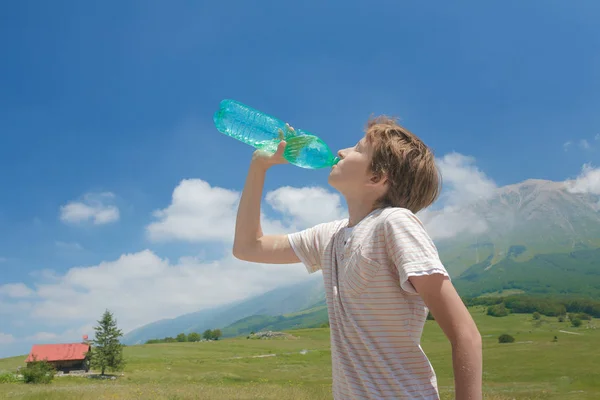 Niño caucásico bebiendo agua clara de la batalla en sus manos en lo alto de los Alpes Imagen de stock
