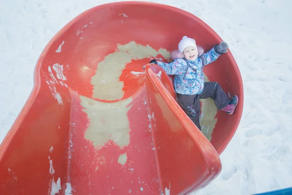 Зимнее веселье маленькой девочки на горке из красного пластика — стоковое фото