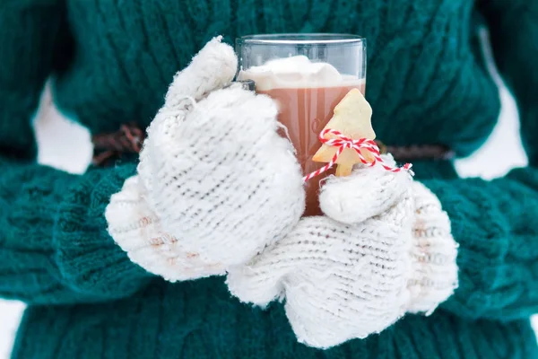 Primer plano de manoplas de mujer que sostienen cacao caliente de Navidad con malvaviscos en taza de vidrio Fotos de stock libres de derechos