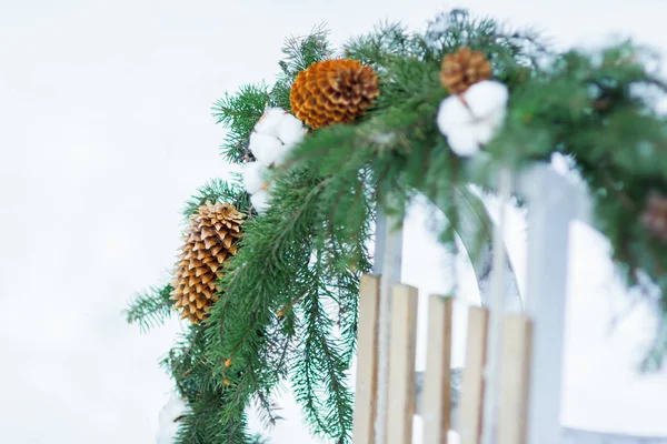 Weihnachtsbaum und Baumwollpflanzenkranz hängen auf Holzschlitten im Freien — Stockfoto