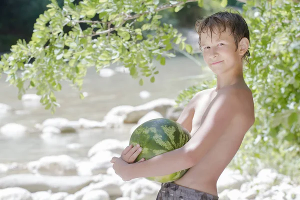 Boy in beach shade holding big green watermelon