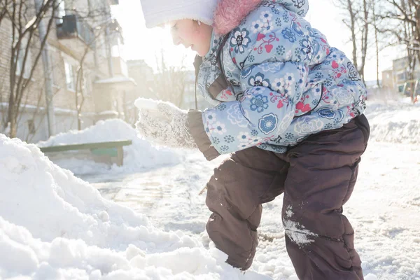 Маленькая девочка в теплой зимней одежде лазает по снегу — стоковое фото