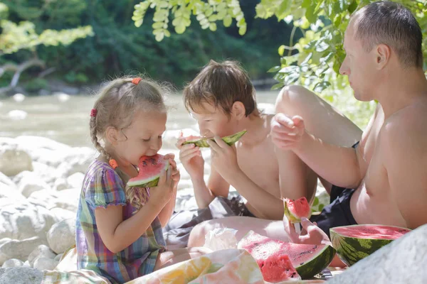 Famiglia di tre persone che mangia fette di anguria fresca in ombra sulla spiaggia — Foto Stock