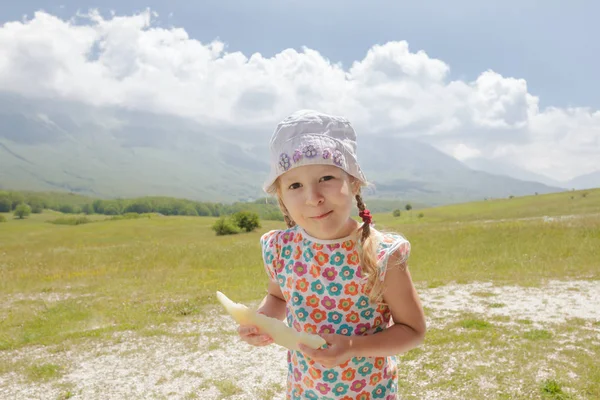 Маленькая девочка с ломтиком дыни в руке наслаждается пребыванием на альпийском лугу — стоковое фото