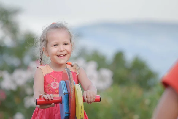 Outdoors holidays of little kid girl swinging on wooden playground equipment — Stock Photo, Image