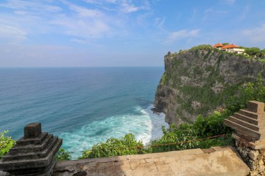 Endonezya 'nın Bali kentindeki Uluwatu uçurumunun manzarası. Pura Luhur Uluwatu Tapınağı 'nın güzel manzarası. Gün boyunca renkli çiçekler ön planda. Yüksek uçurumun manzaralı kıyı manzarası.