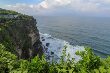 Endonezya 'nın Bali kentindeki Uluwatu uçurumunun manzarası. Pura Luhur Uluwatu Tapınağı 'nın güzel manzarası. Gün boyunca renkli çiçekler ön planda. Yüksek uçurumun manzaralı kıyı manzarası.
