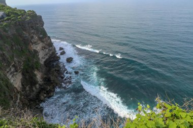 Endonezya 'nın Bali kentindeki Uluwatu uçurumunun manzarası. Pura Luhur Uluwatu Tapınağı 'nın güzel manzarası. Gün boyunca renkli çiçekler ön planda. Yüksek uçurumun manzaralı kıyı manzarası.