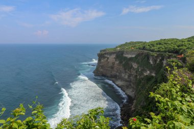 Endonezya 'nın Bali kentindeki Uluwatu uçurumunun manzarası. Pura Luhur Uluwatu Tapınağı 'nın güzel manzarası. Gün boyunca renkli çiçekler ön planda. Yüksek uçurumun manzaralı kıyı manzarası.