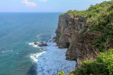Panorama Okyanus Kıyısı 'na bak, Cliff. Çiçek ve yeşil başlıklı dikey uçurum Hint Okyanusu 'nun üzerinde bunaltıcı bir manzara. Bali adasının güneyinde, Pura Luhur Uluwatu Tapınağı. Endonezya.