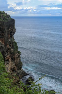 Genel Bakış panorama okyanus kıyısında, cliff. Gün batımı. Bali. Bunalmış sahne çiçek ve Hint Okyanusu üzerinden dikey cliff yeşil şapkalı. Bali Adası Güney Pura Luhur Uluwatu Tapınağı. Endonezya.