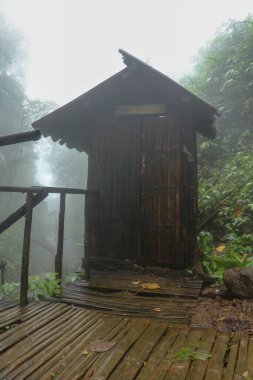 Endonezya 'daki Bali Adası' nda Banyuwana Amerta Sprey Şelalesi. Tropikal ormanda kıyafet değiştirmek için kullanılan bambu binası. Kalın, sütlü beyaz bir sis arka plandaki manzarayı kaplar..