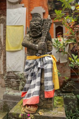 Endonezya, Bali 'deki bir Hindu tapınağının tuğlalı giriş kapısı. Giriş kapısı kapalı. Yanında sarı kurdeleyle bağlanmış, işaretlenmiş malzemeye sarılmış koruyucu bir figür var. Yakın plan..