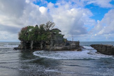 Dalgalar tepesinde Tanah Lot 'un Hindu tapınağı olan bir uçuruma çarpar. Tapınak, Endonezya 'nın Bali adası açıklarında denizde bir kaya üzerine inşa edildi. Uçurumun tepesindeki yemyeşil tropik bitki örtüsü.