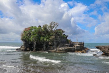 Dalgalar tepesinde Tanah Lot 'un Hindu tapınağı olan bir uçuruma çarpar. Tapınak, Endonezya 'nın Bali adası açıklarında denizde bir kaya üzerine inşa edildi. Uçurumun tepesindeki yemyeşil tropik bitki örtüsü.