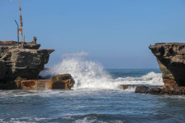 Bali, Endonezya 'da dalgalar dalgaların alçalmasıyla kıyıya çarpıyor. Taşın üzerinde çağlayan su, gelgit havuzunu besliyor. Tanah Lot 'un yakınlarındaki gelgit sırasında dalgalar kayalara vuruyor. Derin mavi okyanus ve gökyüzü arka planda.