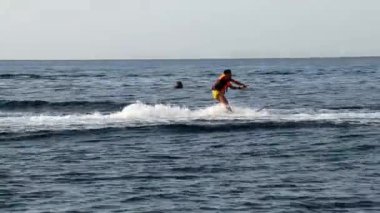 Genç bir adam denizde su kayağı yapıyor. Su kayakçısı su sıçratarak hızla ilerliyor. Denizde sörf yapan bir adam. Genç adam okyanusta su kayağı yapıyor. Sağlıklı bir yaşam tarzı. Bahar ve yaz tatilleri.
