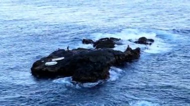 Hint Okyanusu, Bali, Endonezya 'daki kayalık bir uçurumda Balili balıkçılara hava manzarası. Dev dalgalar su sıçratan ve beyaz köpükle kayalara çarpıyor. Su zümrüttür, koyu mavi.