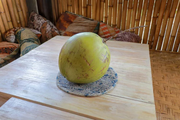 Young green coconut on teak table. Whole coconut with bamboo background and pillow. Healthy tropical fruit from coconut palm. Fresh coconut water.