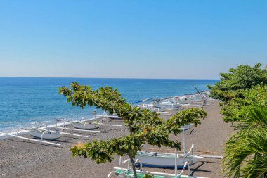 Agung yanardağının yakınındaki siyah volkanik kumsal. Arka planda palmiye ağaçları ve görkemli yanardağı olan tropik bir cennet. Yukarıdan görüntüle.