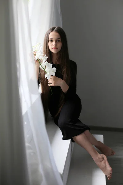 Portrait of european girl sitting by the window with orchid flow — 图库照片