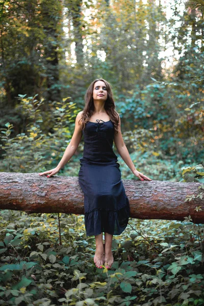 Foto vertical de uma jovem mulher descalça sentada em um tre caído — Fotografia de Stock