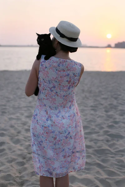 드레스를 모자를 소녀가 카메라를 등지고 해변에 고양이를 — 스톡 사진