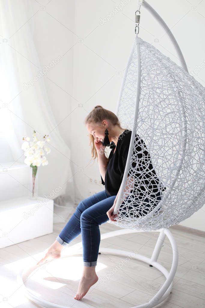 girl with long blond hair sitting in a hanging chair and smiling talking on the phone