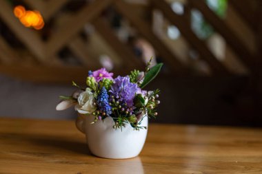 Parlak çiçek aranjmanı beyaz bir tencerede, ahşap bir masada duruyor.