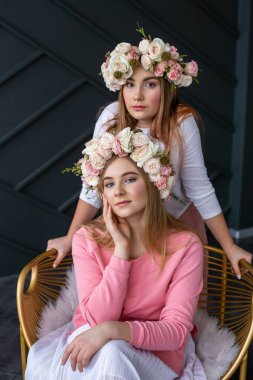 Genç sarışın ve esmer, açık renk elbiseli ve kafalarında narin çelenkler var.