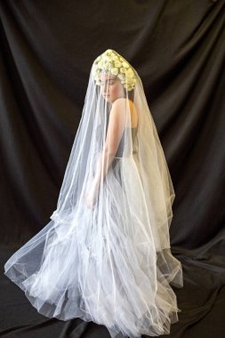 Beyaz pelerinli kız siyah arka planda duruyor.