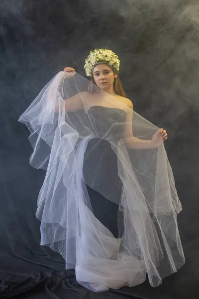a girl stands in a black dress and with a white veil surrounded by haze