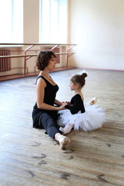 little ballerina sits on a twine together with a teacher in a ballet class