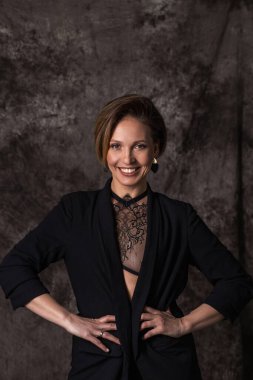 Siyah takım elbiseli genç bir kadın gülümseyerek kazanan bir poz veriyor ve doğrudan kameraya bakıyor.