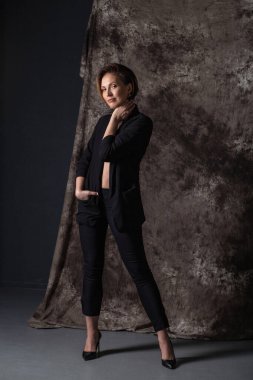 Siyah takım elbiseli, yüksek topuklu ayakkabılı genç ve güzel bir kadın kameraya bakıyor.