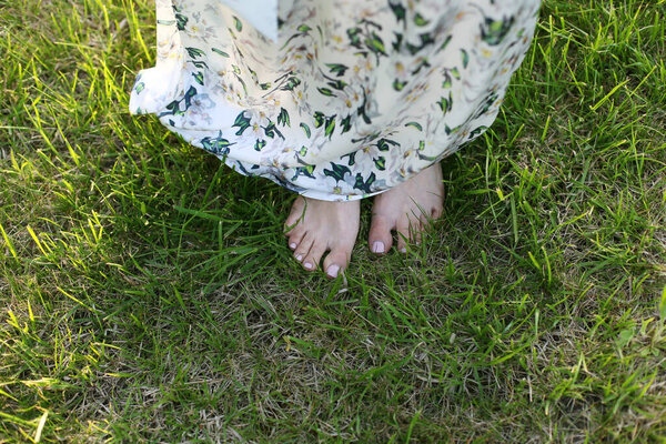 Young woman in a beautiful long dress stands barefoot on green grass on a warm summer day