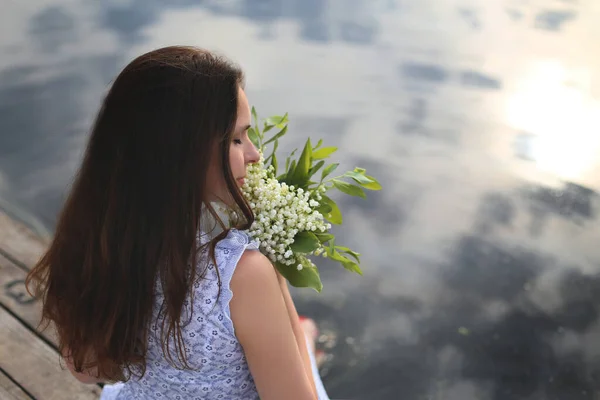 一个黑头发的年轻女子 手里拿着一束花 坐在码头上 — 图库照片