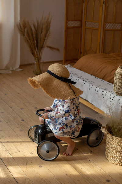 a girl in a funny straw hat rides a childs car around the room