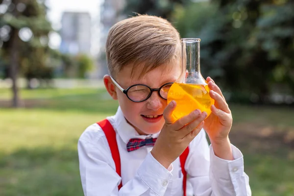 six-year-old boy intently examines a chemical flask with an unknown bright yellow solution