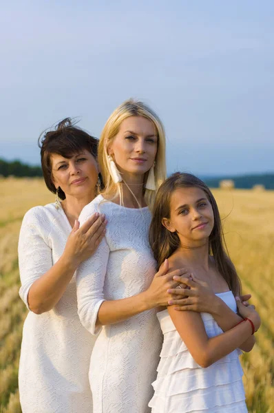 一位50岁的母亲和她的两个身着白衣的女儿在麦田边拍照 并看着摄像机 — 图库照片