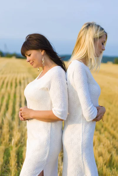 a thirty-five-year-old daughter and her fifty-year-old mother in white dresses stand in the field with their backs to each other