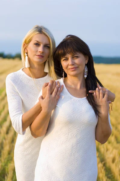 lovely older and younger women in white dresses and beautiful earrings stand and look at the camera